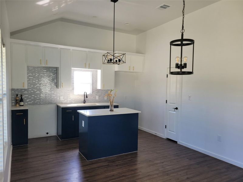 Kitchen featuring two tone cabinets, a center island, dark wood-style flooring, decorative backsplash, and lofted ceiling