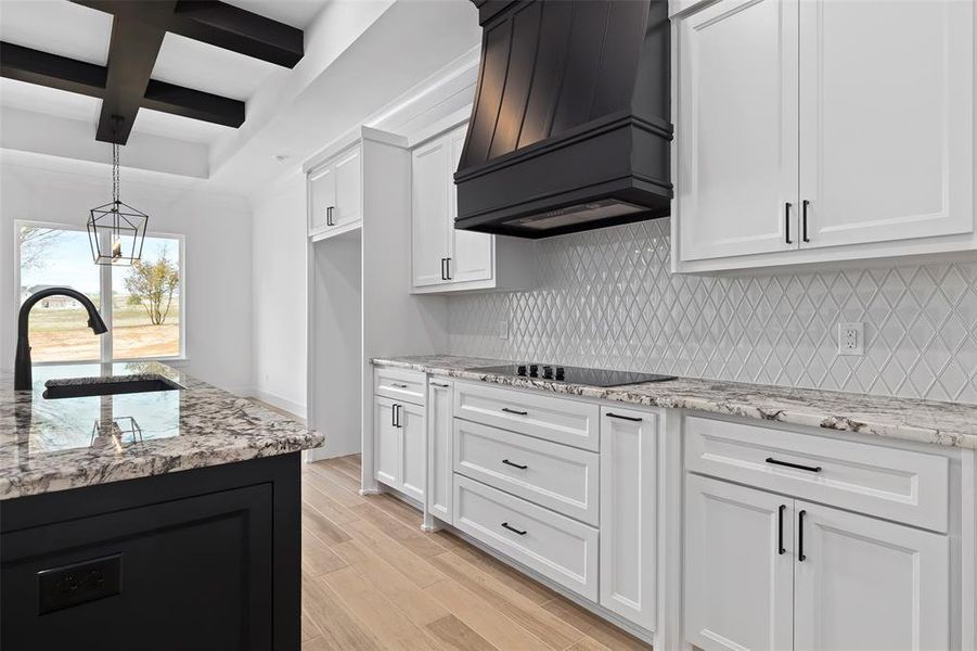 Kitchen featuring custom range hood, beam ceiling, coffered ceiling, light wood-type flooring, and light stone countertops