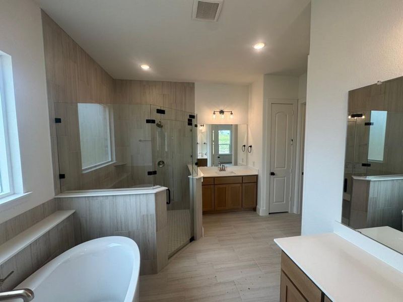 Spacious bathroom featuring a freestanding soaking tub, a frameless glass shower enclosure, wood-look tile flooring, and dual vanity areas with white countertops