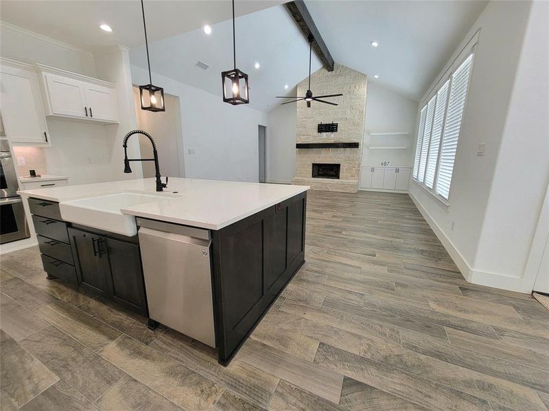 Kitchen with a fireplace, sink, a center island with sink, dishwasher, and white cabinets