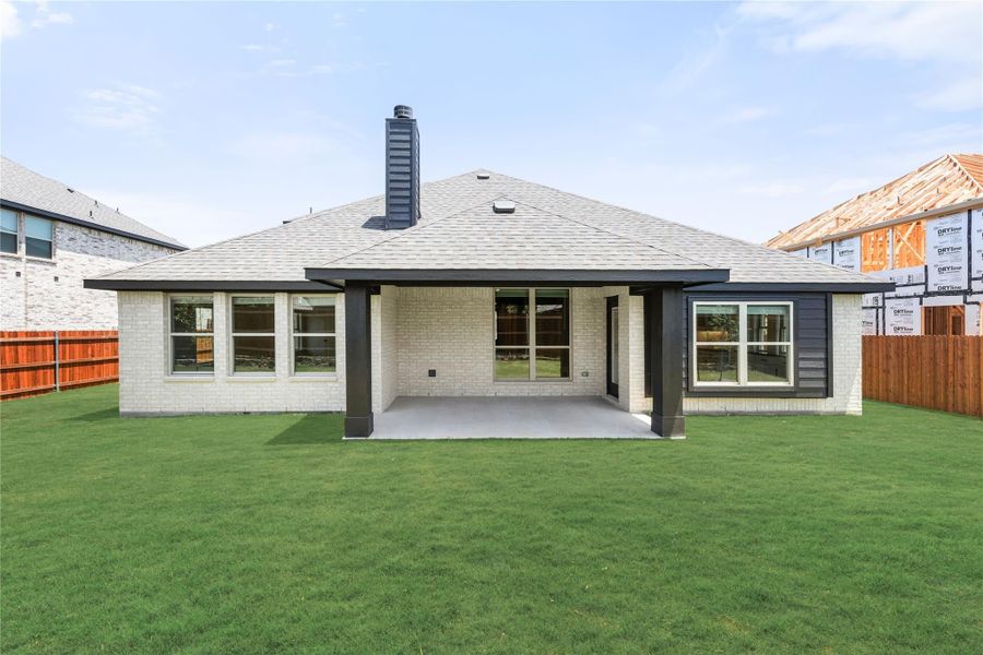 Rear exterior of single-story brick home with covered patio, chimney, and green backyard lawn