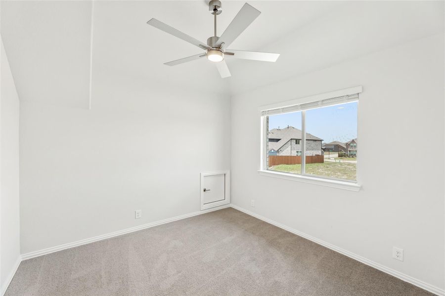 Empty bedroom with vaulted ceiling, ceiling fan, carpet flooring, and a window overlooking neighboring homes Empty bedroom with vaulted ceiling, ceiling fan, carpet flooring, and a window overlooking neighboring homes