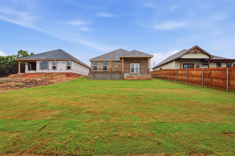 Expansive green lawn with a newly constructed brick and siding home featuring a covered patio and a wood privacy fence Expansive green lawn with a newly constructed brick and siding home featuring a covered patio and a wood privacy fence