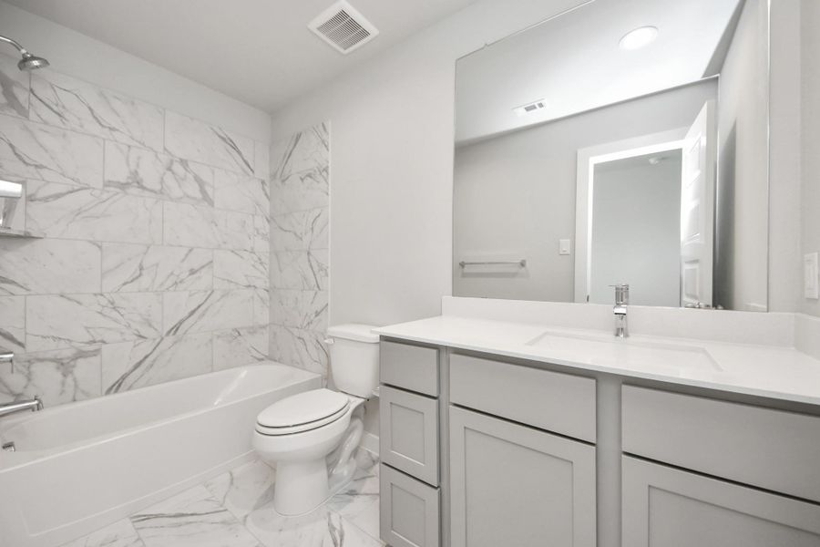 Secondary bath features tile flooring, bath/shower combo with tile surround, light stained wood cabinets, beautiful light countertop. Sample photo of completed home with similar floor plan. Actual colors and selections may vary.
