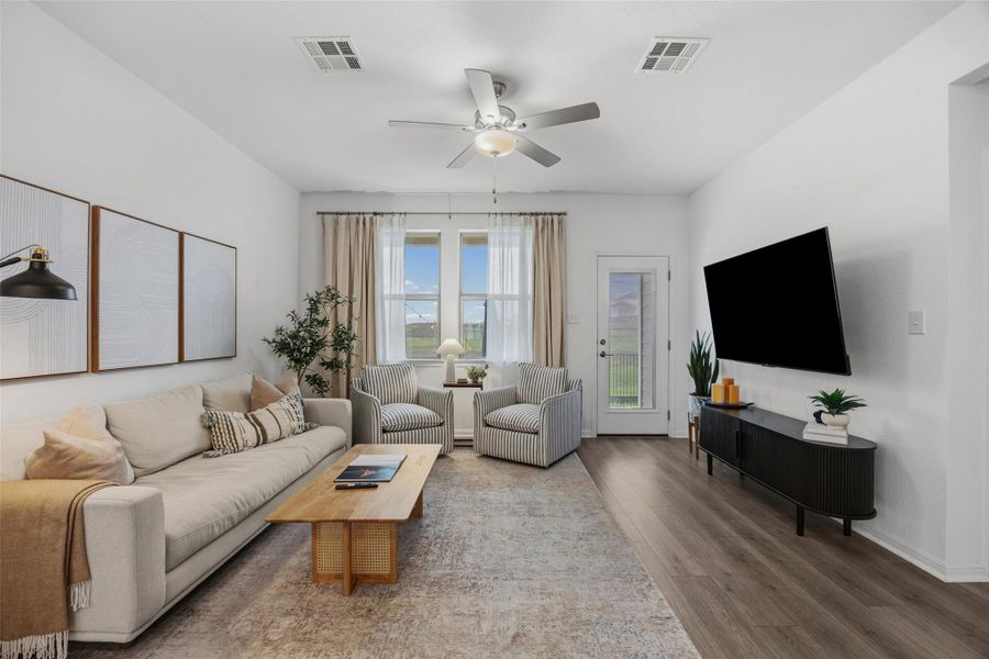 Bright living area featuring wood-finish flooring, a contemporary ceiling fan, and large windows with sheer and blackout curtains
