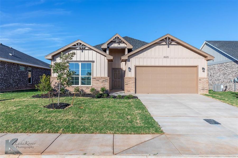 View of front of house with board and batten siding, driveway, a garage, a front lawn, and brick.
