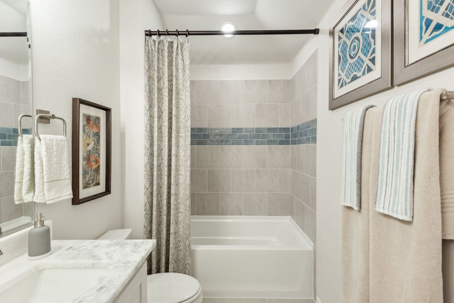 Bathroom with tiled tub and shower, marble vanity countertop, and gray curtain rod