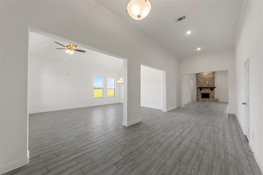 Unfurnished living room featuring wood finished floors, crown molding, ceiling fan, baseboards, and a brick fireplace