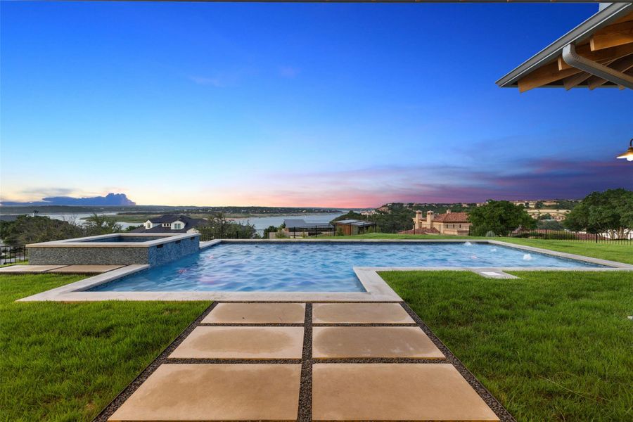 Pool at dusk with a patio area, a pool with connected hot tub, and a water view