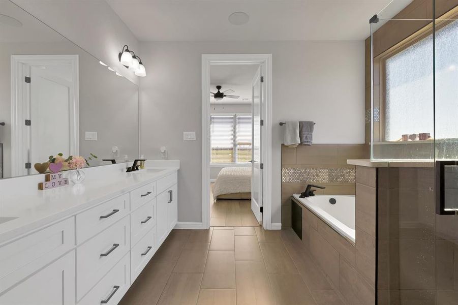 Ensuite bathroom featuring double vanity, connected bathroom, a ceiling fan, a bath, and a sink