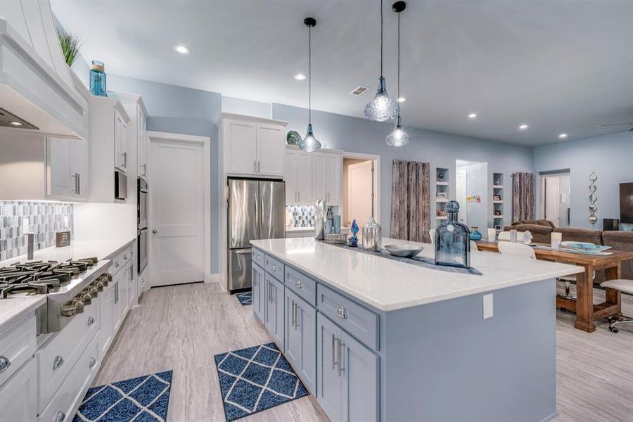 Kitchen featuring white cabinetry, stainless steel appliances, tasteful backsplash, decorative light fixtures, and custom range hood