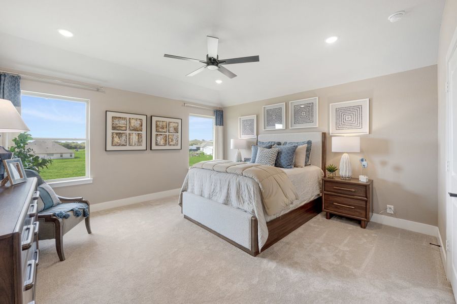 Spacious bedroom with wood bed frame, ceiling fan, carpet flooring, and two large windows with outdoor views.