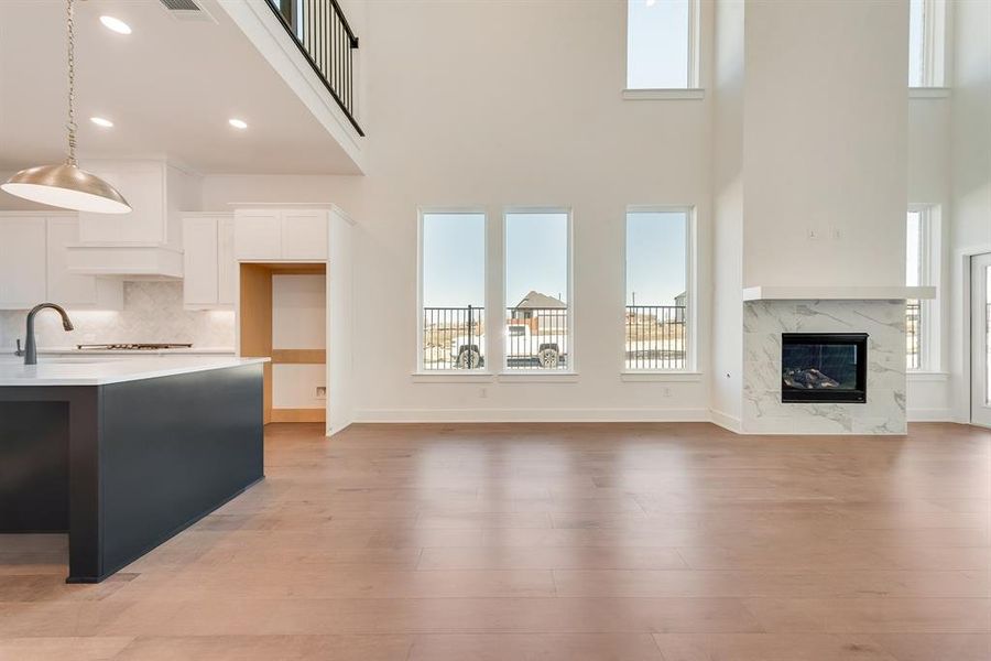 Unfurnished living room featuring a premium fireplace, light wood-style flooring, a towering ceiling, and recessed lighting Unfurnished living room featuring a premium fireplace, light wood-style flooring, a towering ceiling, and recessed lighting