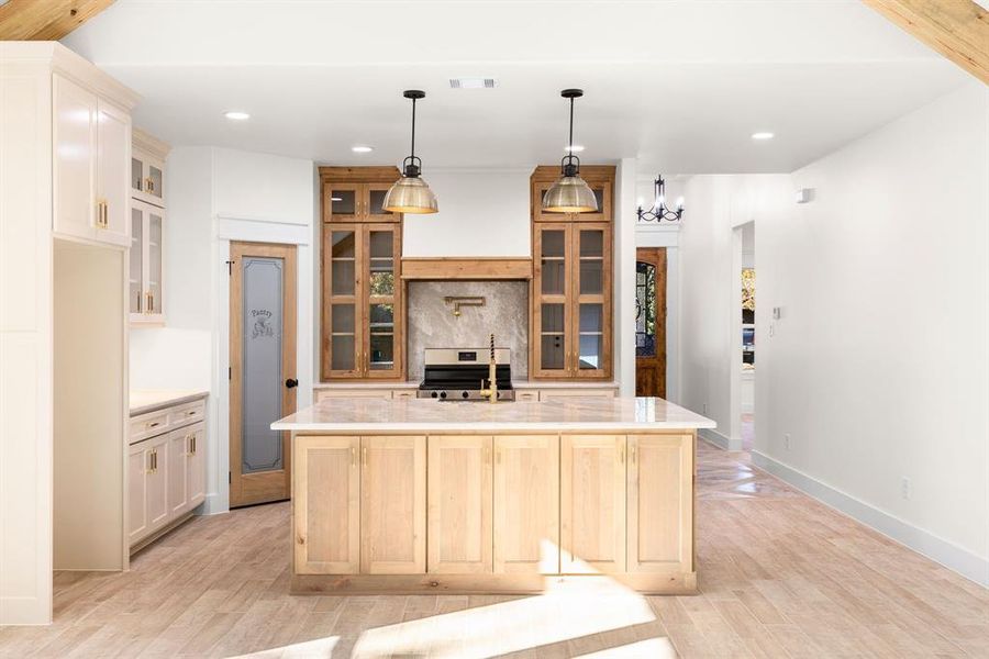 Kitchen featuring backsplash, a center island with sink, hanging light fixtures, stainless steel range, and light hardwood / wood-style floors