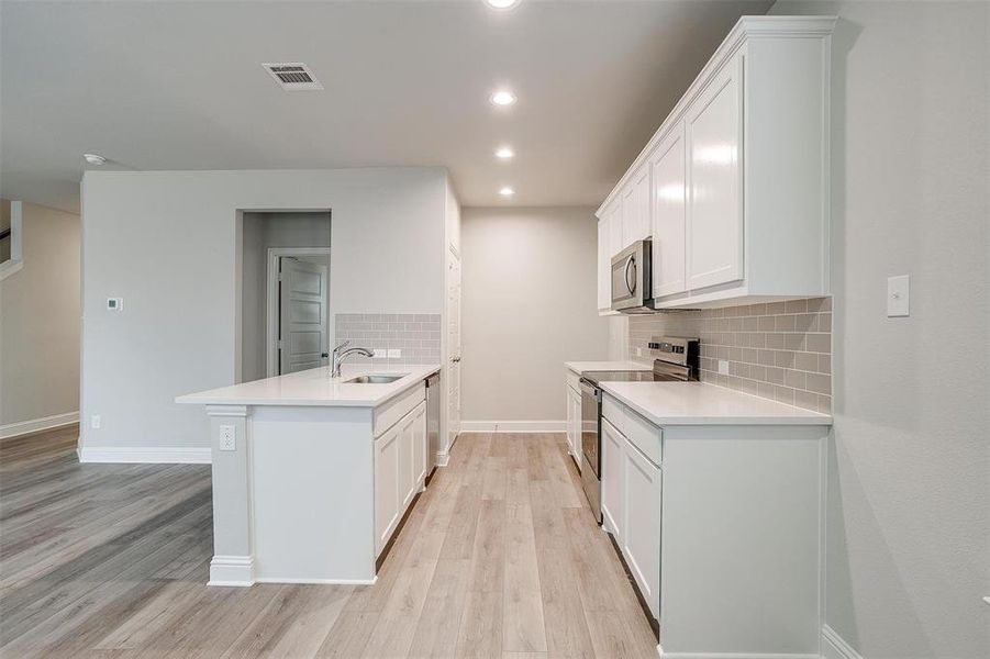 Kitchen with white cabinetry, light hardwood / wood-style flooring, stainless steel appliances, and kitchen peninsula