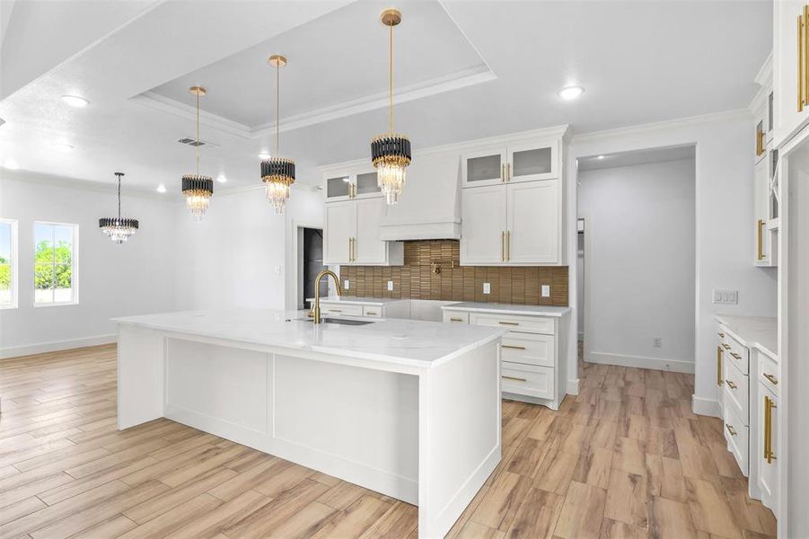 Kitchen with ornamental molding, light stone counters, a raised ceiling, glass insert cabinets, and white cabinets
