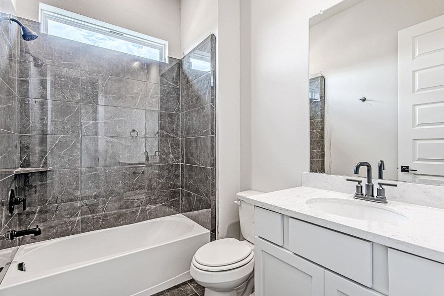 A secondary first-floor bathroom featuring elegant gray tile surround, a transom window for soft natural light, and modern matte black fixtures.