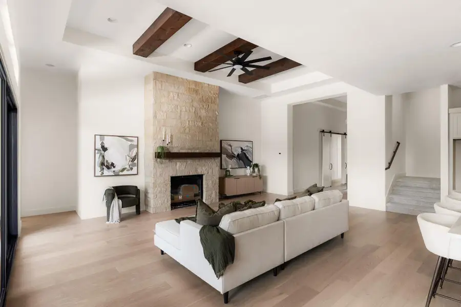 An inviting living area with a stone fireplace, exposed wooden beams, and elegant hardwood flooring.