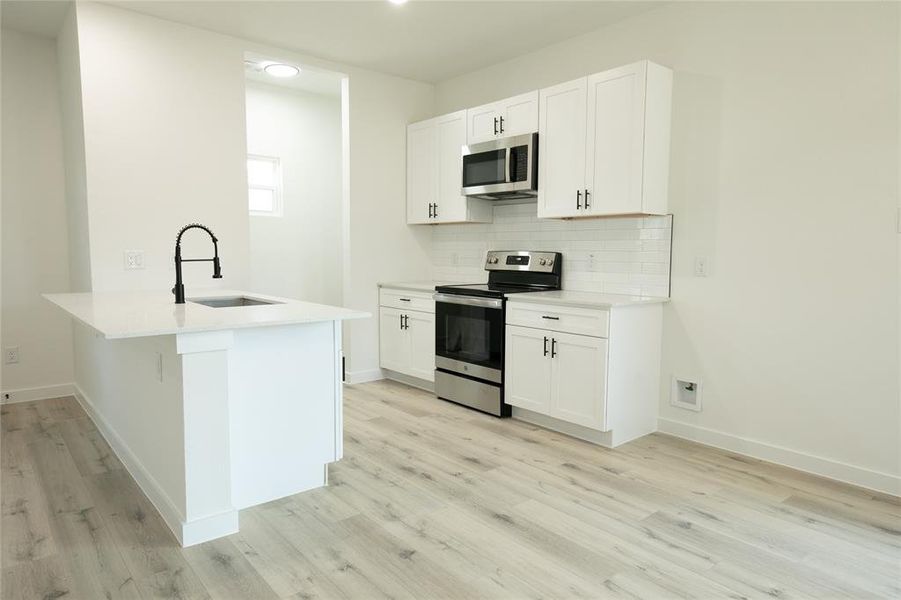 Kitchen with white cabinetry, kitchen peninsula, appliances with stainless steel finishes, backsplash, and sink