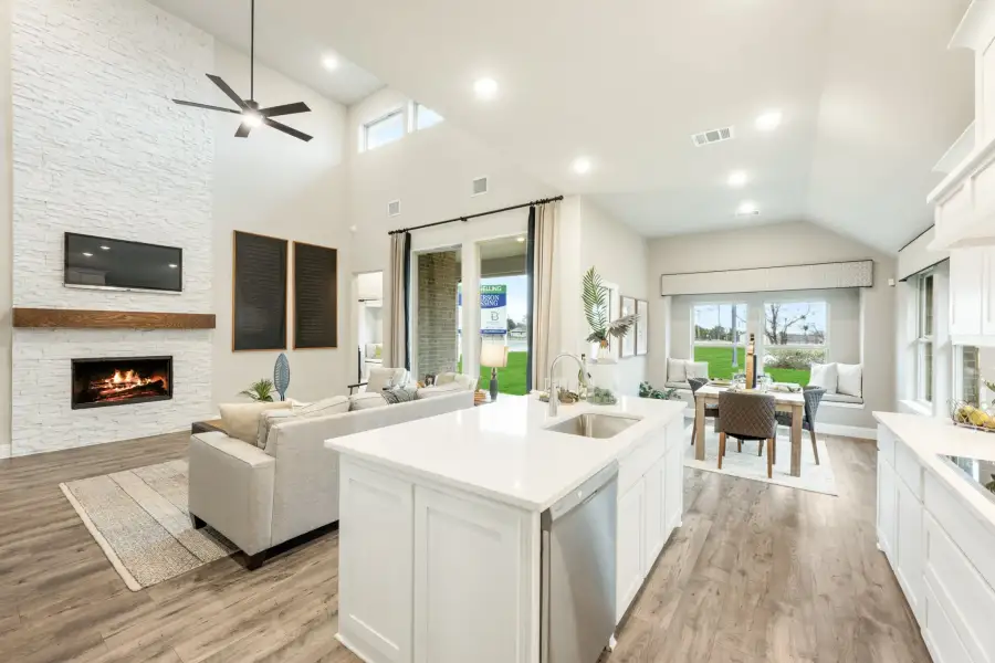 Open-concept living area with kitchen island, stone fireplace, vaulted ceiling, and hardwood floors