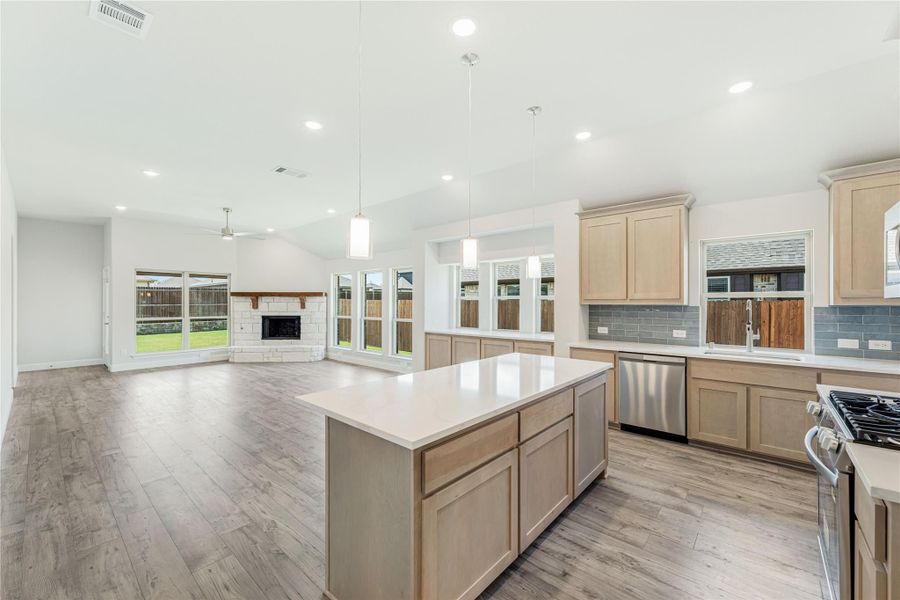 Open kitchen with center island, light wood cabinets, and blue tile backsplash, open to living room with fireplace Open kitchen with center island, light wood cabinets, and blue tile backsplash, open to living room with fireplace