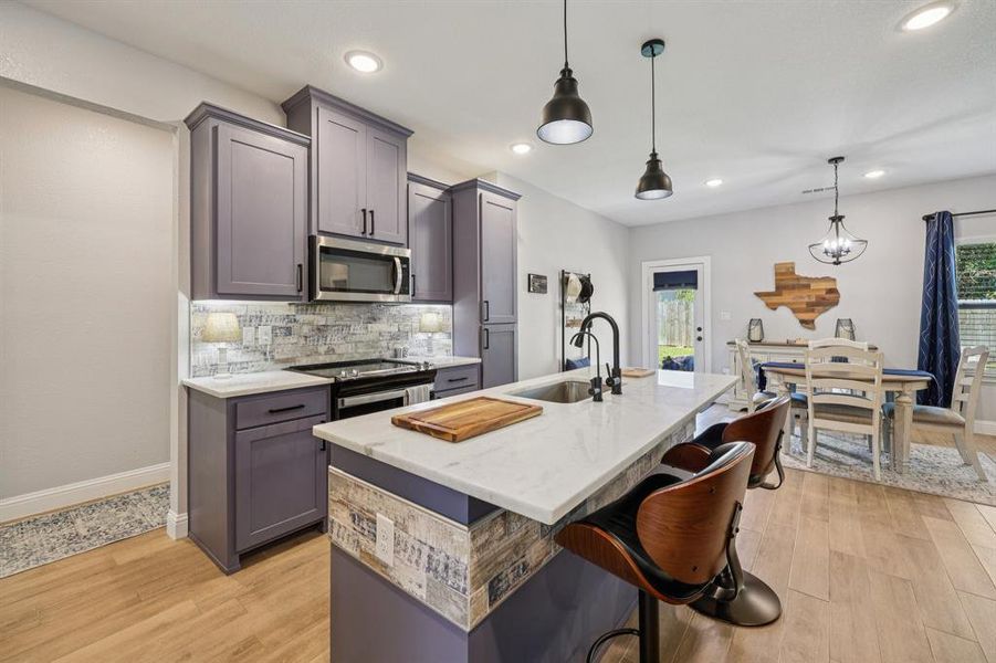 Kitchen featuring a breakfast bar, hanging light fixtures, backsplash, a center island with sink, and stainless steel microwave Kitchen featuring a breakfast bar, hanging light fixtures, backsplash, a center island with sink, and stainless steel microwave