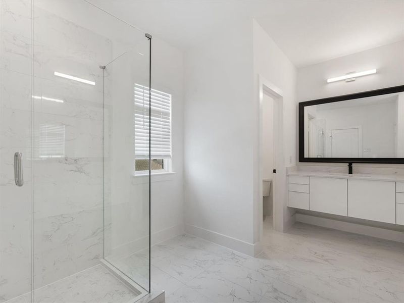Primary Bathroom featuring light marble finish flooring, a marble finish shower, and vanity