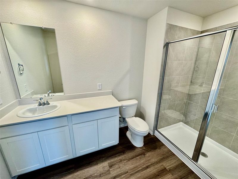 Full bath featuring vanity, wood finished floors, a stall shower, and a textured wall Full bath featuring vanity, wood finished floors, a stall shower, and a textured wall