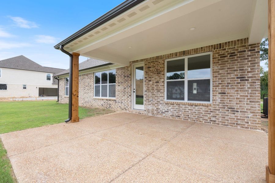 Covered patio featuring an exposed aggregate concrete surface, brick exterior, white-framed windows, and a glass-paneled door Covered patio featuring an exposed aggregate concrete surface, brick exterior, white-framed windows, and a glass-paneled door