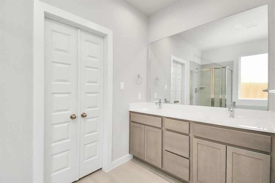 The primary bathroom is located alongside a spacious walk-in closet with shelving, high ceilings, custom paint, and sleek, dark modern finishes. An ideal retreat for unwinding after a long day! Example photo of completed home with similar plan. Actual may vary.