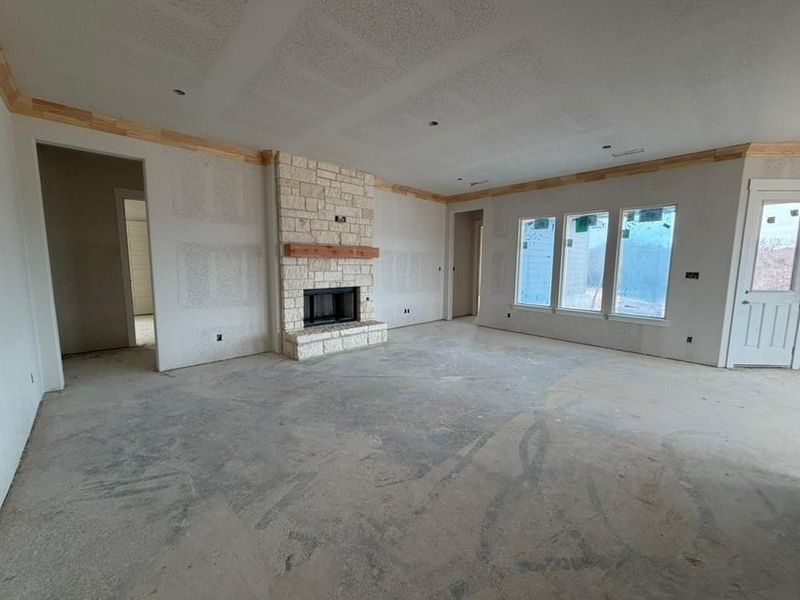 Unfurnished living room with a stone fireplace, ornamental molding, concrete floors, and a textured ceiling Unfurnished living room with a stone fireplace, ornamental molding, concrete floors, and a textured ceiling
