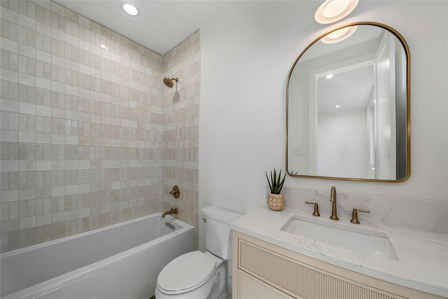 Bathroom featuring a tub and shower combination with vertical-set tile surround, a single vanity with stone-finish countertop, and a contemporary arched mirror with a brass-tone frame