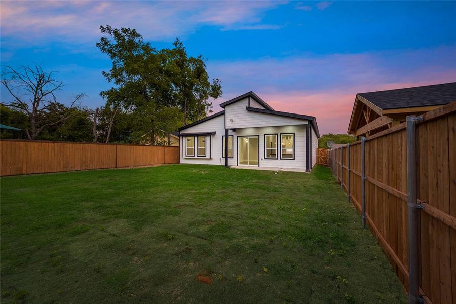 Back house at dusk featuring a lawn