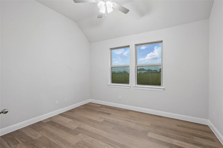 Empty room featuring vaulted ceiling, light wood finished floors, and ceiling fan Empty room featuring vaulted ceiling, light wood finished floors, and ceiling fan