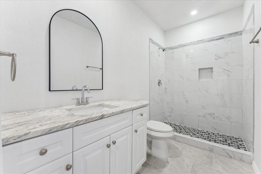 Bathroom with tiled shower, vanity, and toilet