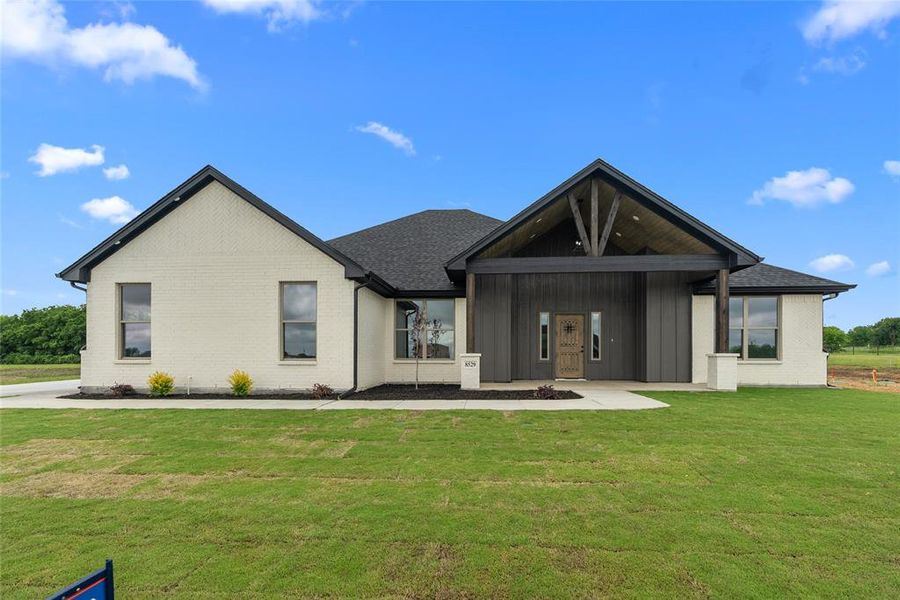 Back of house featuring a lawn, board and batten siding, brick siding, and roof with shingles