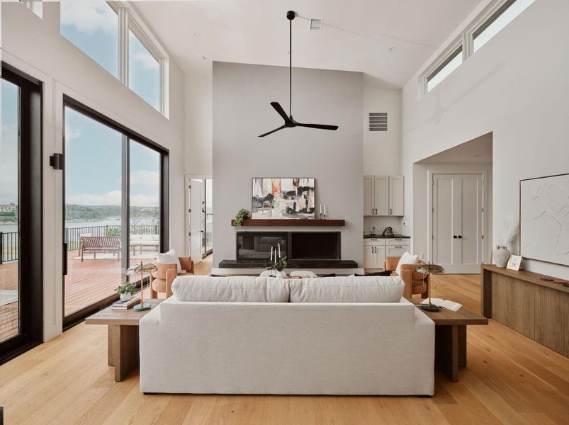 Vaulted living space featuring an expansive sliding glass door system, high ceilings, wood-finish flooring, a contemporary fireplace with a wood mantle, and a built-in wet bar