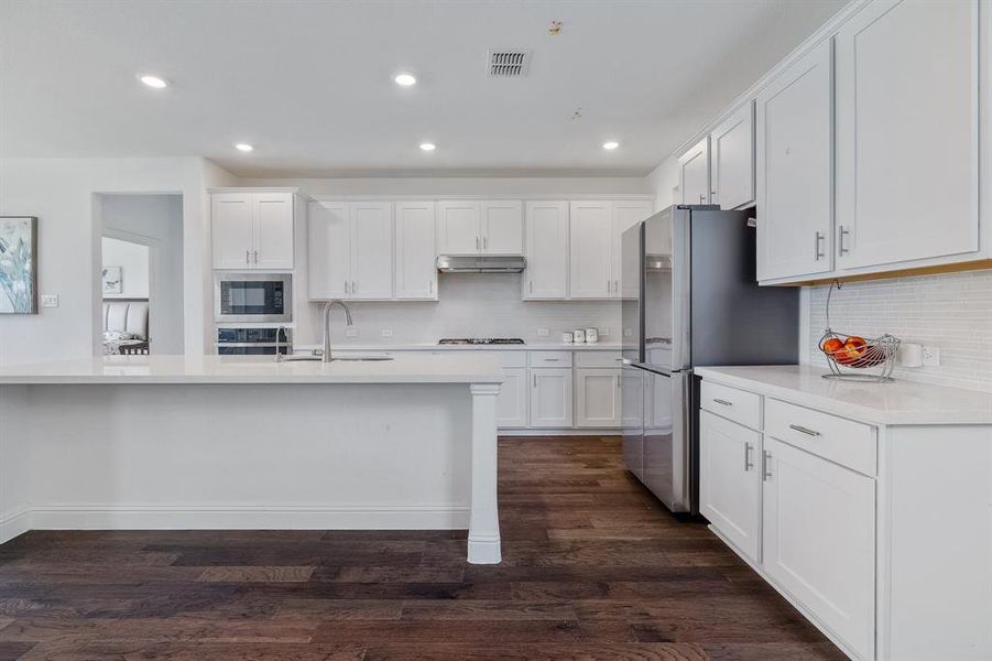 Kitchen with visible vents, stainless steel appliances, under cabinet range hood, white cabinetry, and a sink