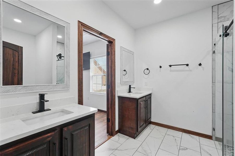 Full bathroom with light marble finish flooring, two vanities, a marble finish shower, and recessed lighting Full bathroom with light marble finish flooring, two vanities, a marble finish shower, and recessed lighting