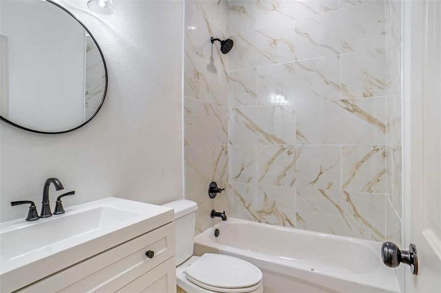 Full bathroom featuring vanity, tiled shower / bath combo, and toilet