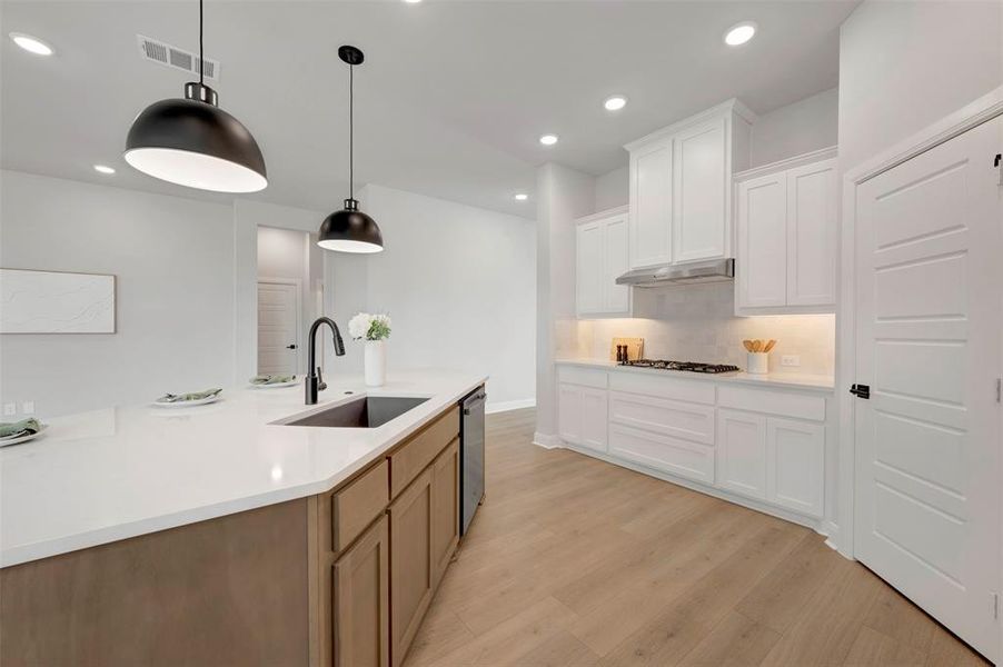 Kitchen with dual tone cabinetry, light wood-style flooring, decorative light fixtures, backsplash, and light stone counters
