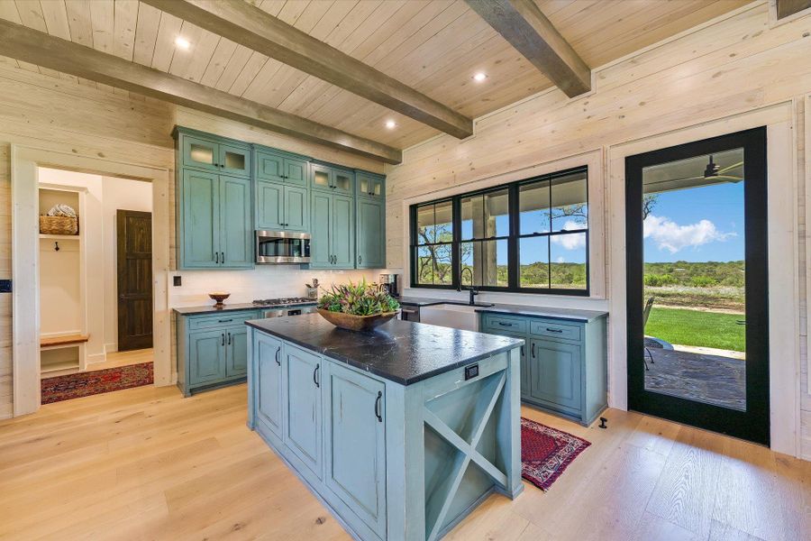 Kitchen featuring light wood finished floors, glass insert cabinets, a center island, green cabinetry, and stainless steel microwave