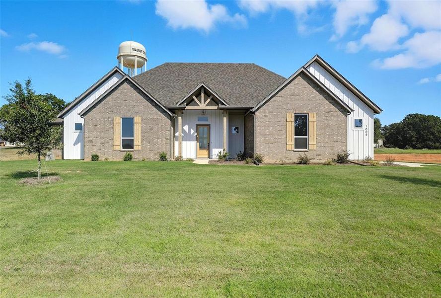 View of front of house with board and batten siding, a front yard, brick siding, and covered porch View of front of house with board and batten siding, a front yard, brick siding, and covered porch