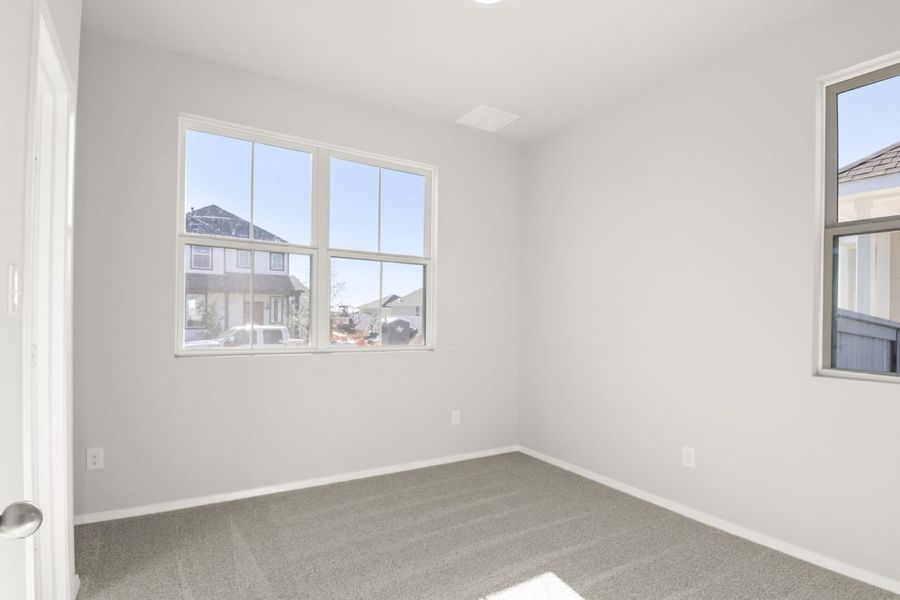 Image of a bedroom with tan carpeting and light grey walls with a large window