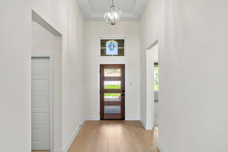 Foyer featuring a dark wood-finish entry door with four frosted glass panels, a clear transom window, and a decorative ceiling light fixture Foyer featuring a dark wood-finish entry door with four frosted glass panels, a clear transom window, and a decorative ceiling light fixture