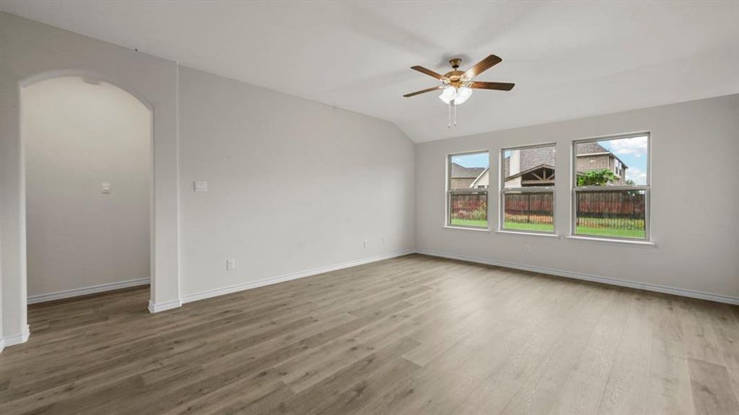 Spacious living area featuring wood-finish flooring, a ceiling fan, and three large windows
