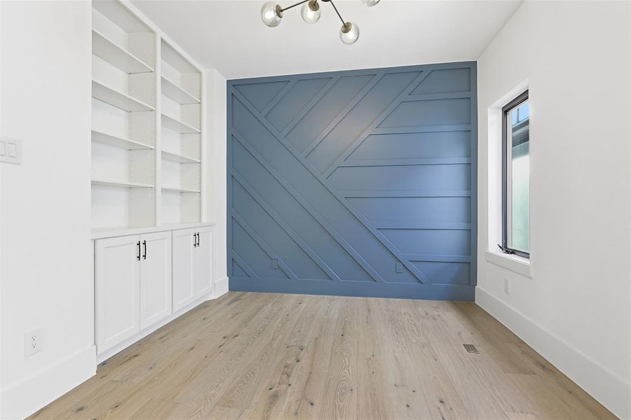 This versatile bonus room highlights a geometric wood-panel accent wall in a slate blue finish and built-in white cabinetry.
