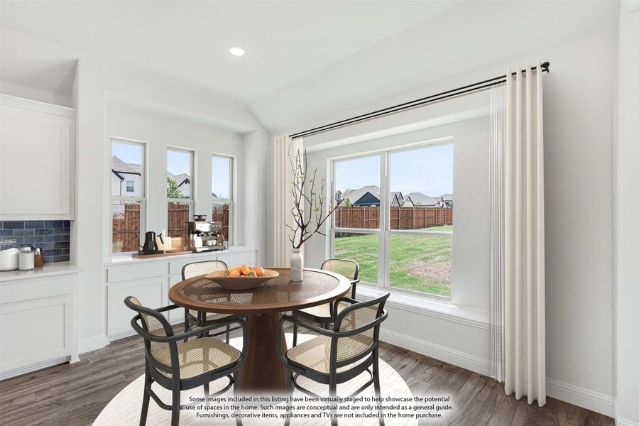 Bright dining nook with round wood table, four chairs, large windows, and hardwood floors next to white kitchen cabinets.