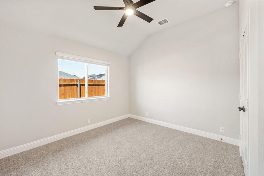 Empty bedroom with vaulted ceiling, ceiling fan, carpet flooring, and single window overlooking backyard fence Empty bedroom with vaulted ceiling, ceiling fan, carpet flooring, and single window overlooking backyard fence