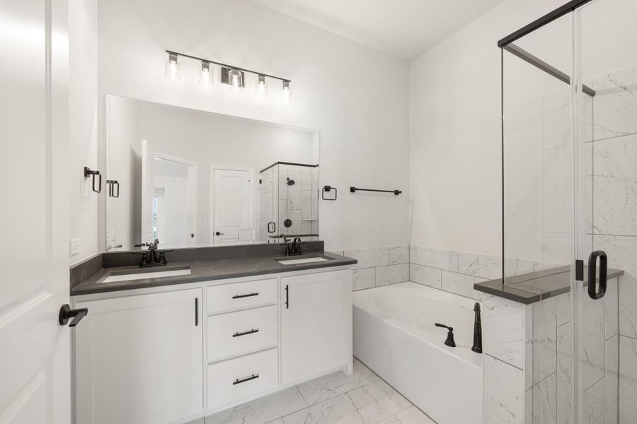 Bathroom with double sink vanity, soaking tub, glass shower, white cabinets, and dark countertops